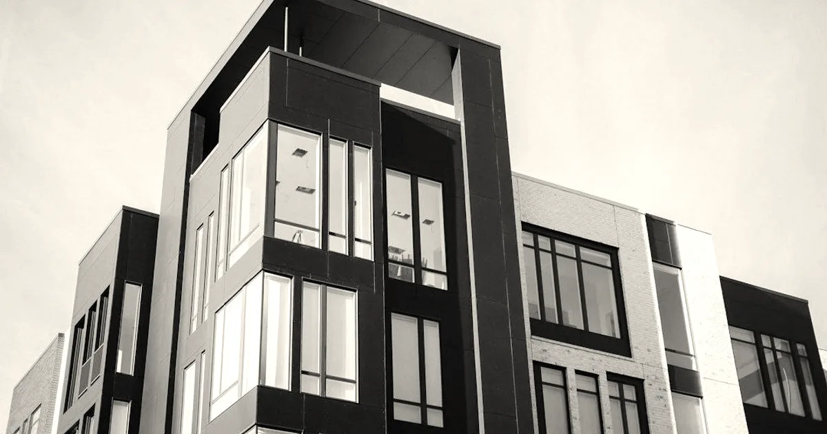 Modern multi-story residential apartment building exterior with dark and light panels under a blue sky