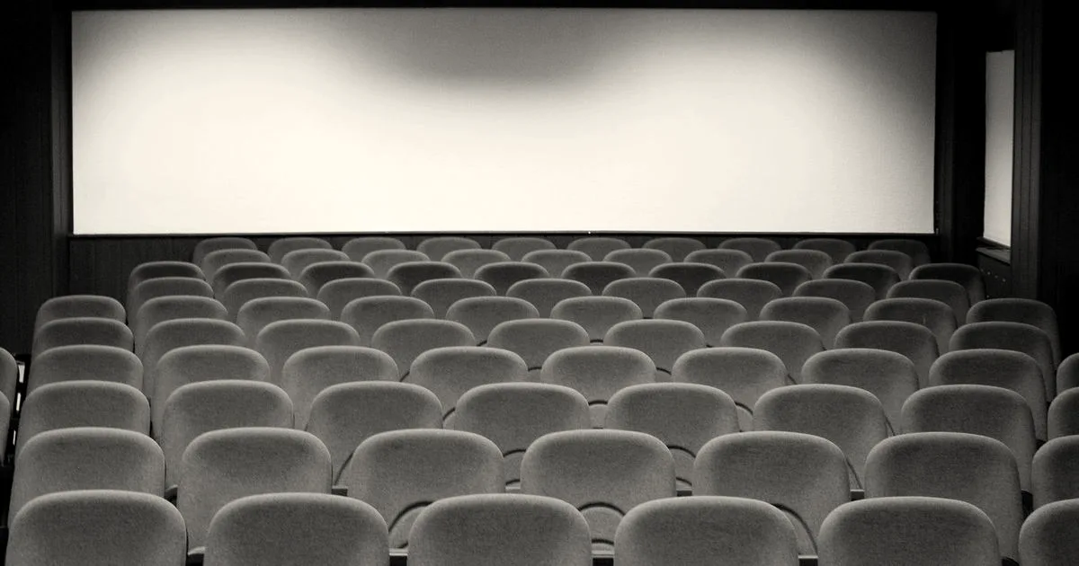 An empty movie theater auditorium with rows of red velvet seats facing a large blank projection screen