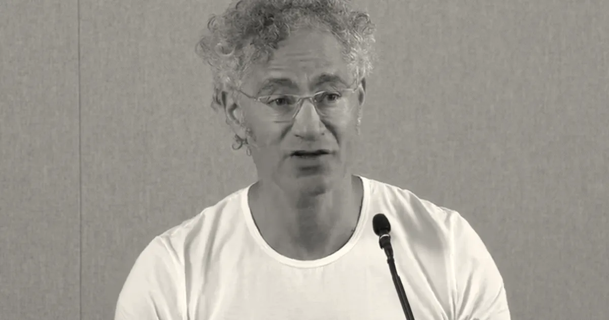 Palantir CEO Alex Karp speaking into a microphone in front of a blue background.
