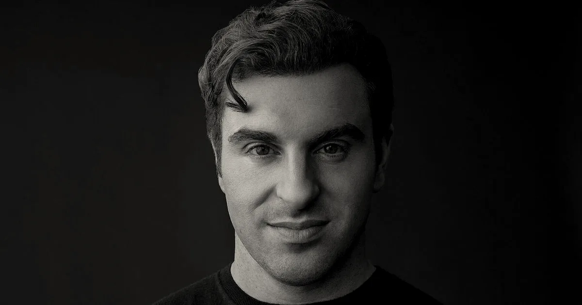 Portrait of a man with dark curly hair, wearing a black sweater, arms crossed, smiling slightly