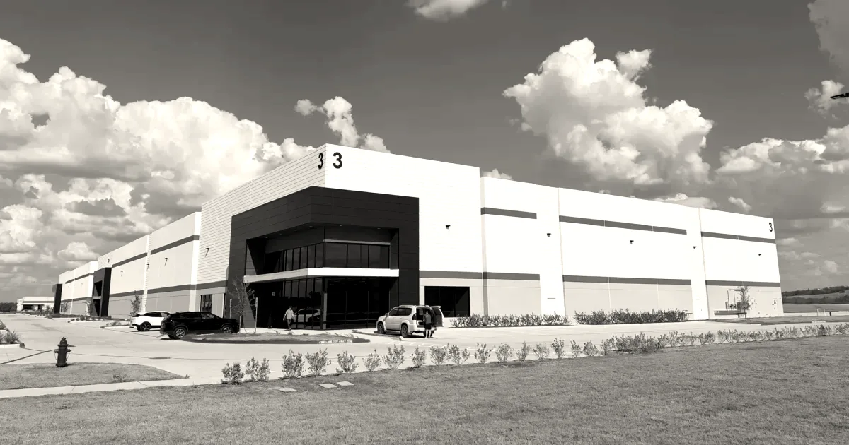 Exterior view of a large white industrial warehouse facility under a blue sky with clouds.