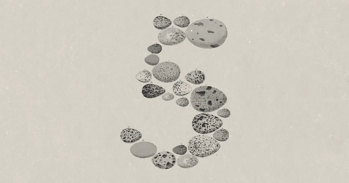 The numeral 5 spelled out using a collection of various colored stones on a beige background