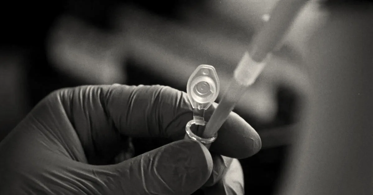 Gloved hand pipetting orange liquid into a microcentrifuge tube in a laboratory environment