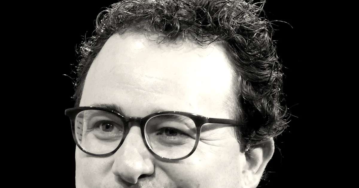 Portrait of Dario Amodei wearing glasses and a blue shirt, smiling during an event.