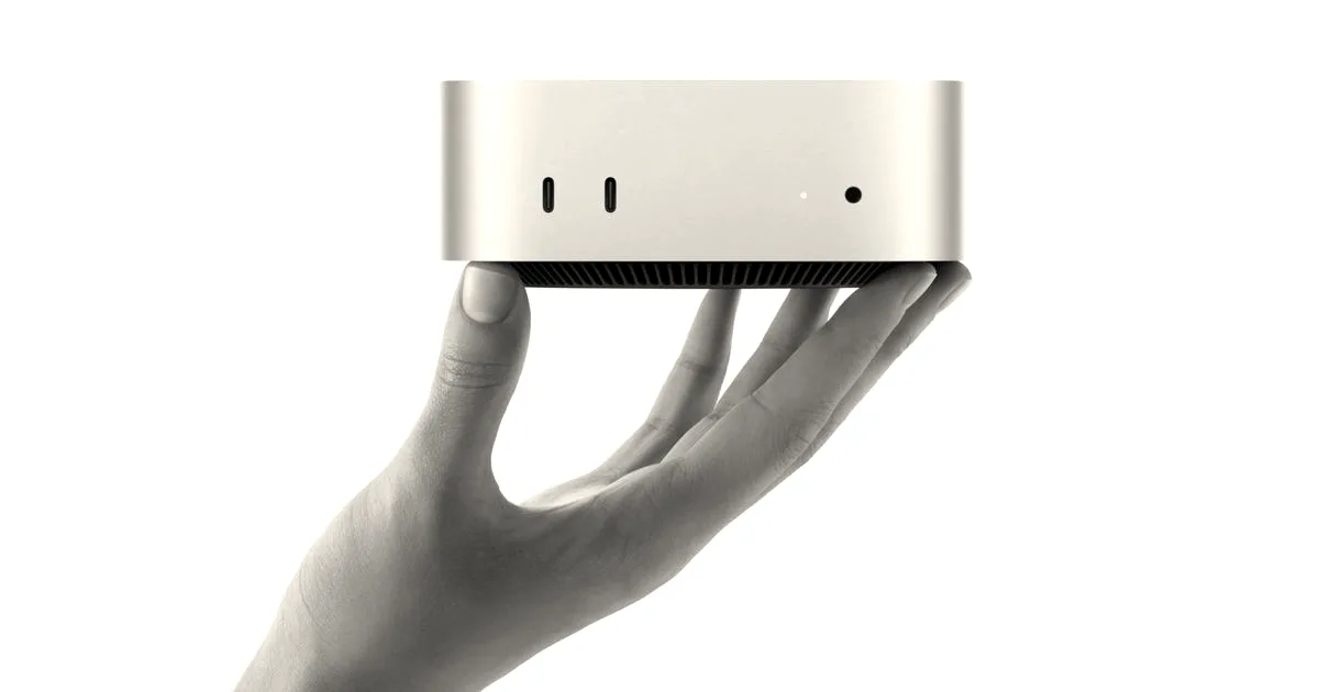 A person's hand holding up a compact, silver Apple Mac Mini desktop computer.