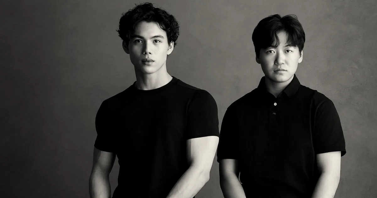 Two men wearing black shirts sitting against a dark gray background in a portrait setup.