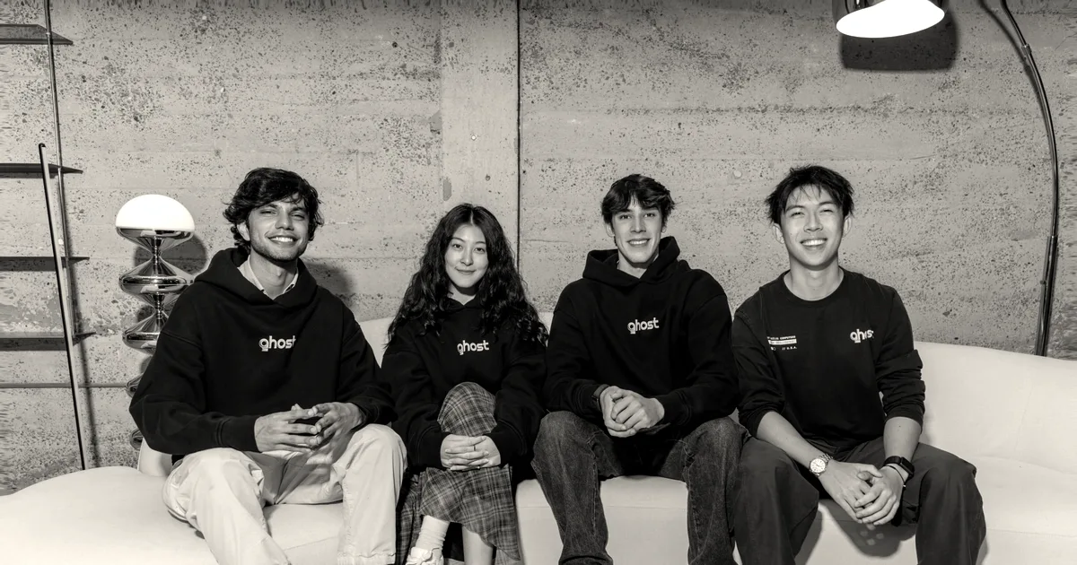 Four members of the Ghost team wearing branded black hoodies and sitting together on a white couch