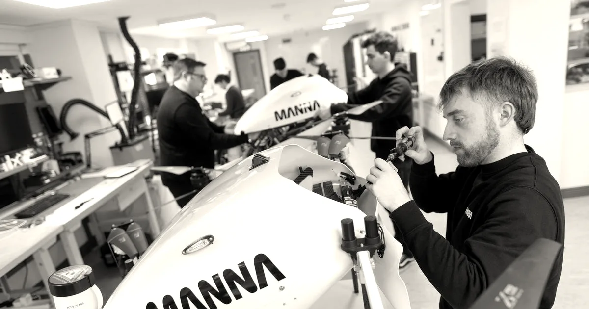 Technician assembles a white Manna delivery drone in a workshop as others work in background