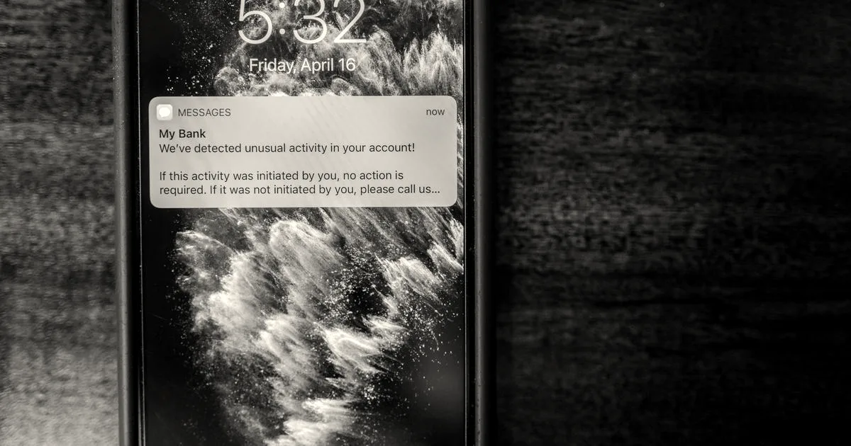Smartphone on a wooden desk displaying an account alert notification about unusual bank activity.