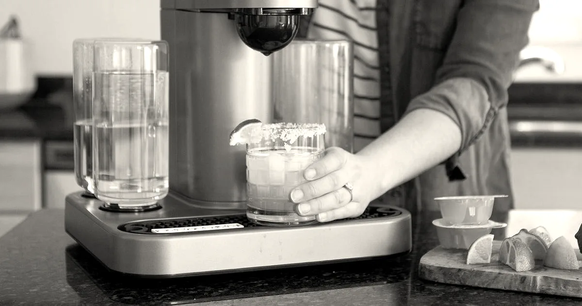 A person taking a freshly prepared cocktail from a Bartesian automatic cocktail maker on a kitchen counter.