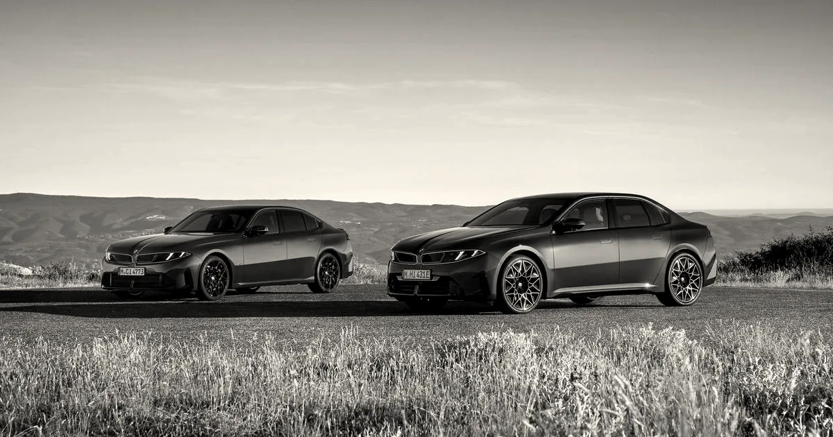 A red BMW and a blue BMW sedan parked side by side on an open road overlooking hills