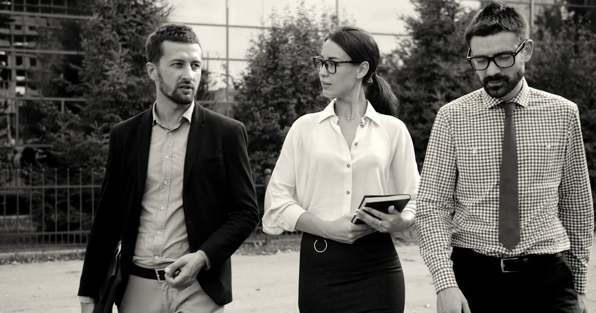 Three business professionals walking and discussing ideas outdoors in a modern urban setting.