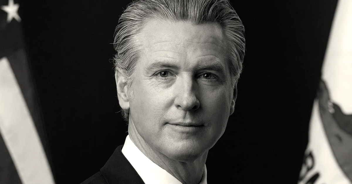 Official portrait of California Governor Gavin Newsom in a dark suit against state and American flags