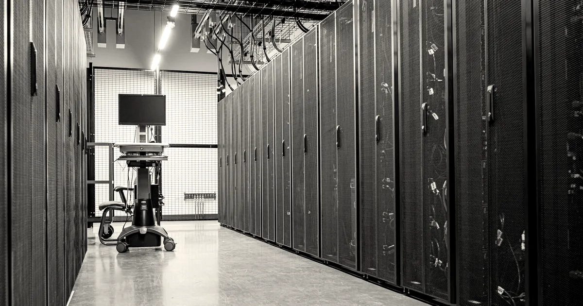 Spacious aisle inside a contemporary data center lined with tall black server rack enclosures and overhead wiring