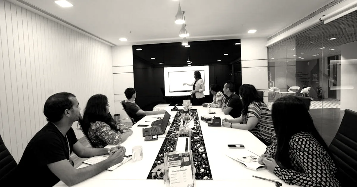 A business team gathered around a long conference table during a presentation in a modern office.