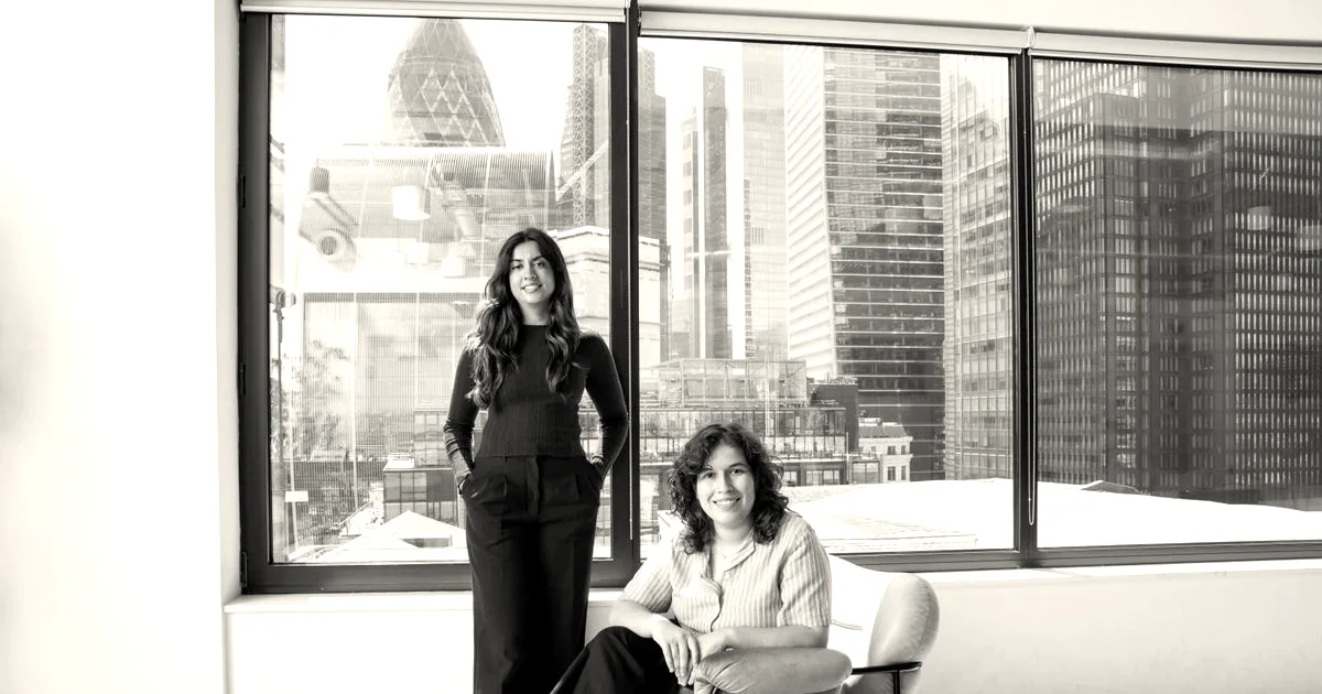 Two women founders of Cascade standing in front of a large office window with a city skyline view.