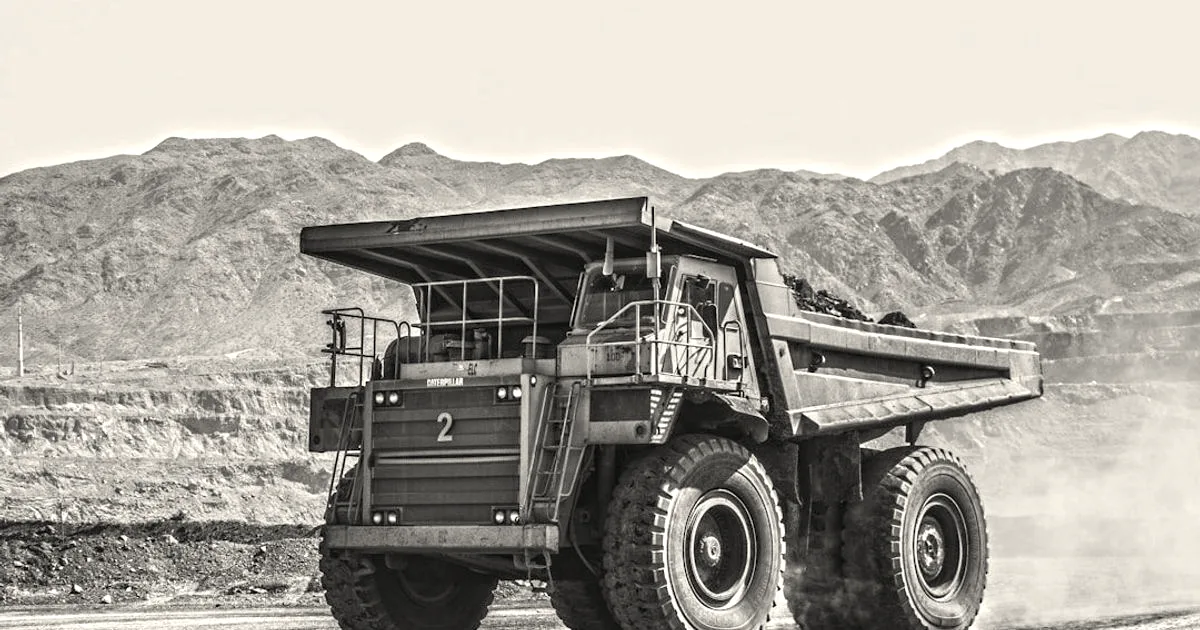 A massive Caterpillar yellow mining dump truck driving through an open-pit mine site.