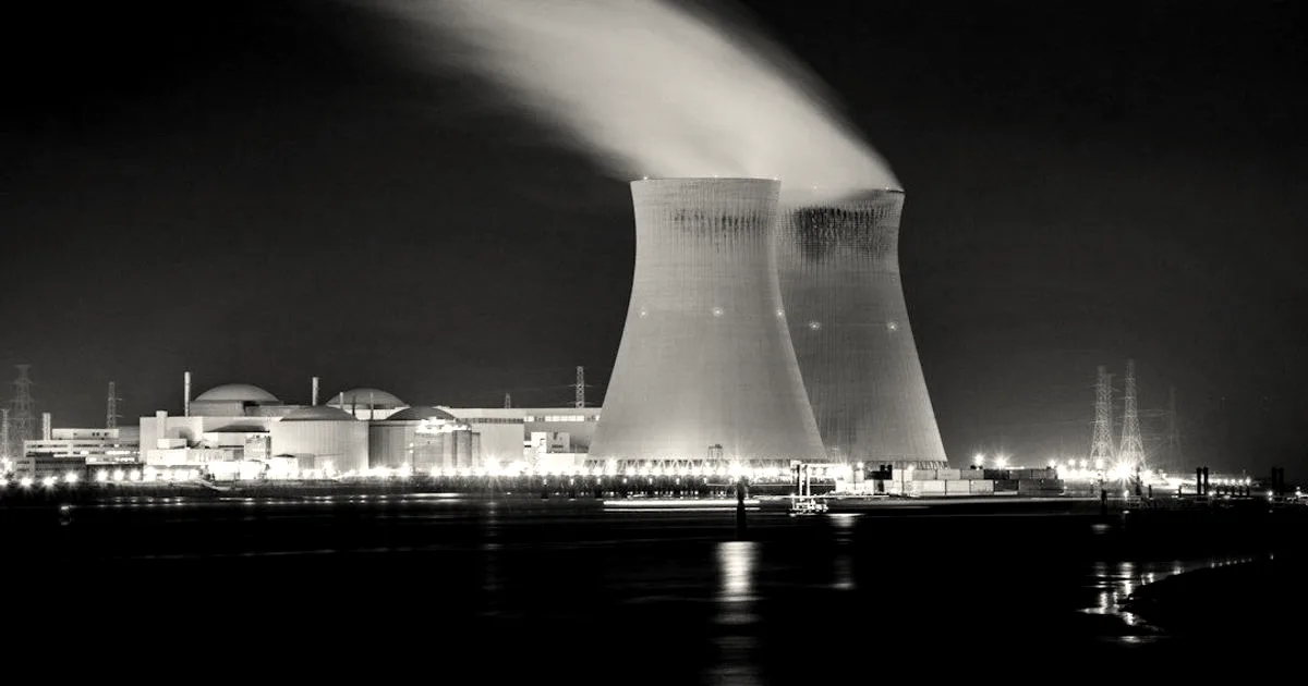 Illuminated nuclear power plant at night with steam billowing from two cooling towers across water