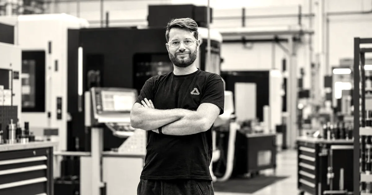 Theo Saville, co-founder of CloudNC, standing with arms crossed in front of manufacturing machinery.