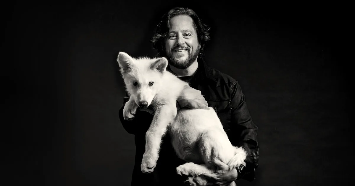 Ben Lamm, co-founder and CEO of Colossal Biosciences, holding a white wolf pup against a dark background.