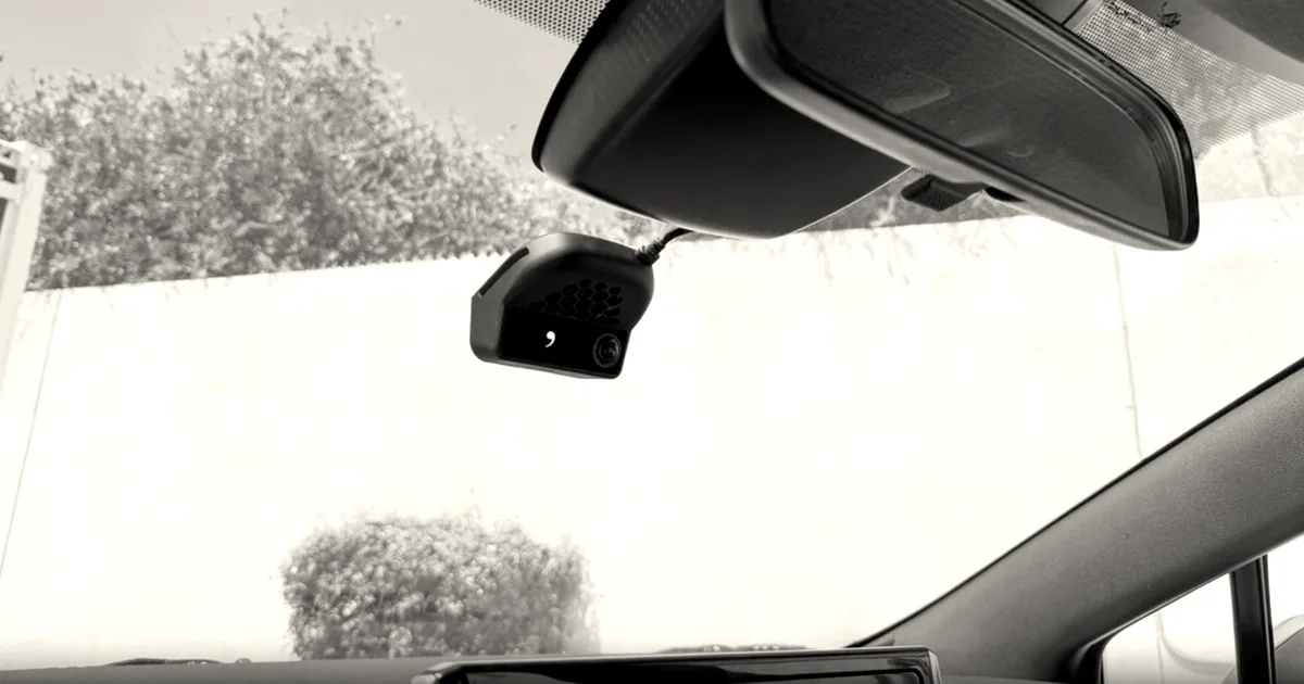 A Comma driver-assist device mounted beneath the rearview mirror on the windshield of a car interior.