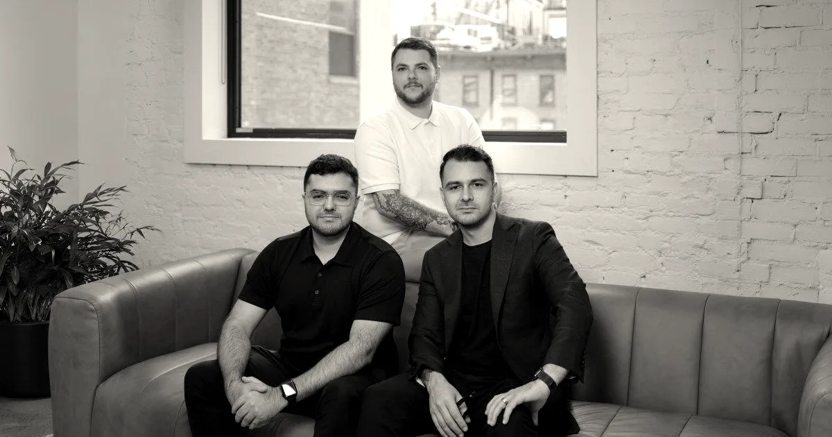 Three team members of Comp AI sitting together in an office setting with brick walls.