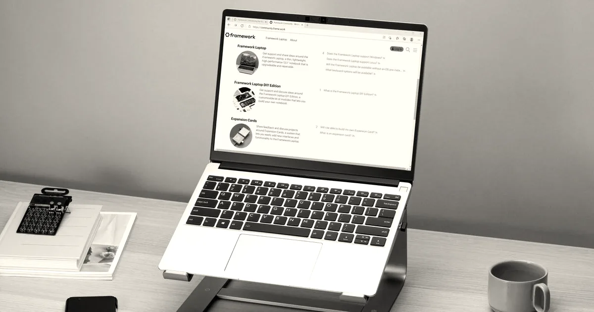 A Framework laptop resting on a desk stand next to a notepad and coffee mug.
