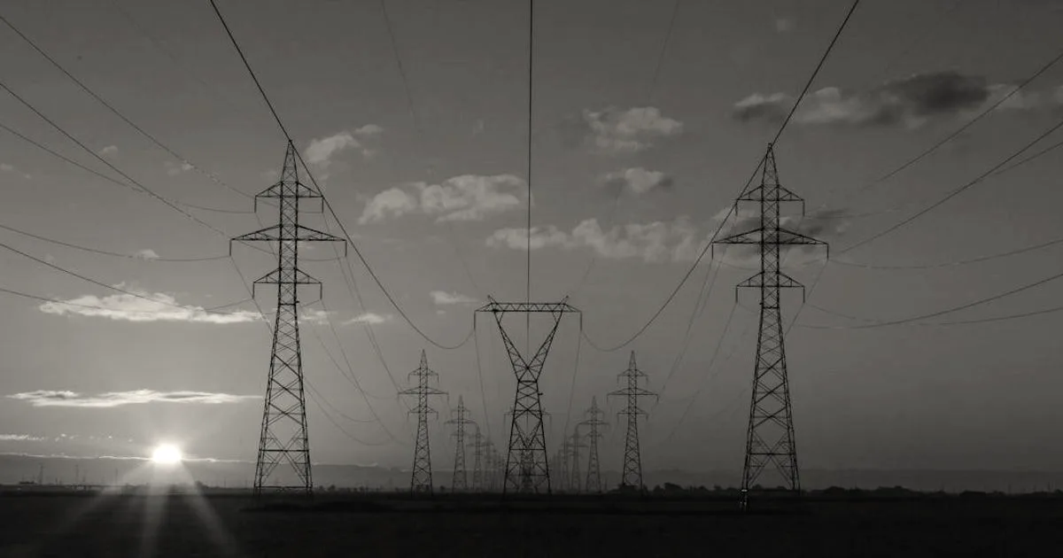 A row of power transmission towers stretching into the distance against a vibrant sunset sky.