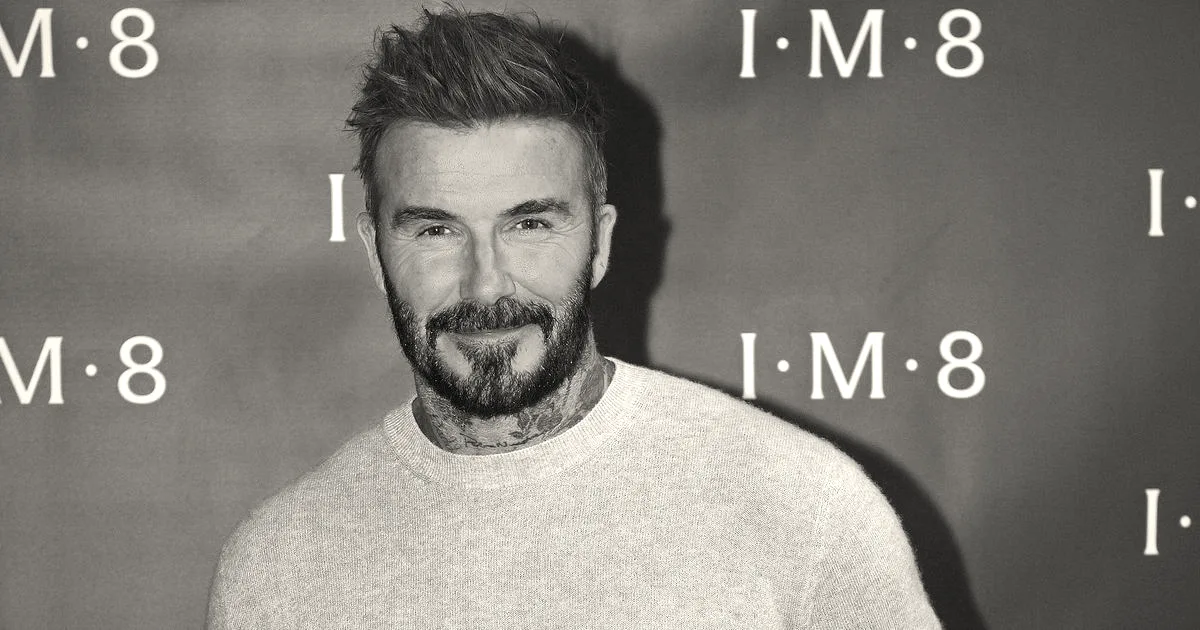 David Beckham smiling in front of a red backdrop featuring the IM8 brand logo.