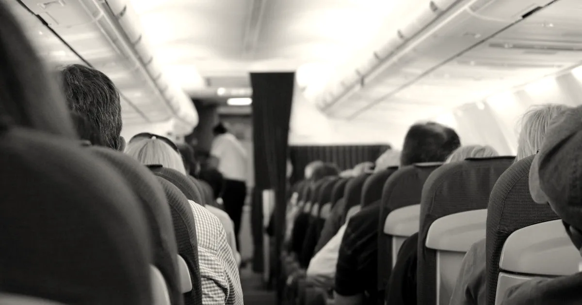 Passengers seated inside an airplane cabin looking toward the front during a flight.