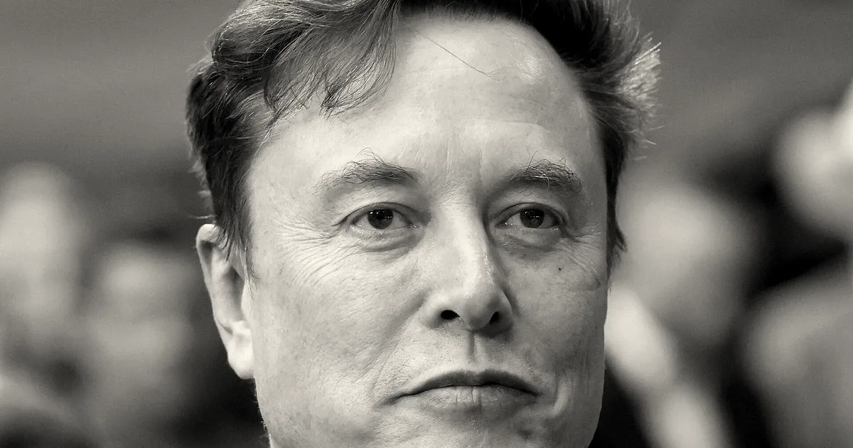 Close-up portrait of Elon Musk in a dark suit and tie looking at the camera