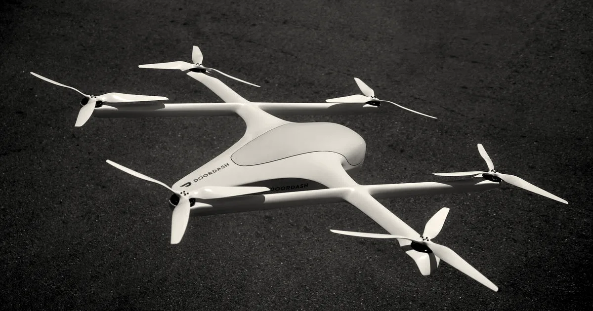 A white DoorDash delivery drone with multiple propellers rests on an asphalt surface.