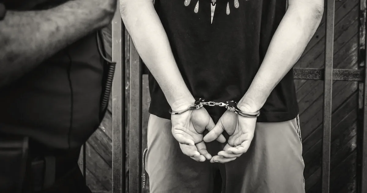 Close-up of a person in handcuffs standing in front of an officer during an arrest.
