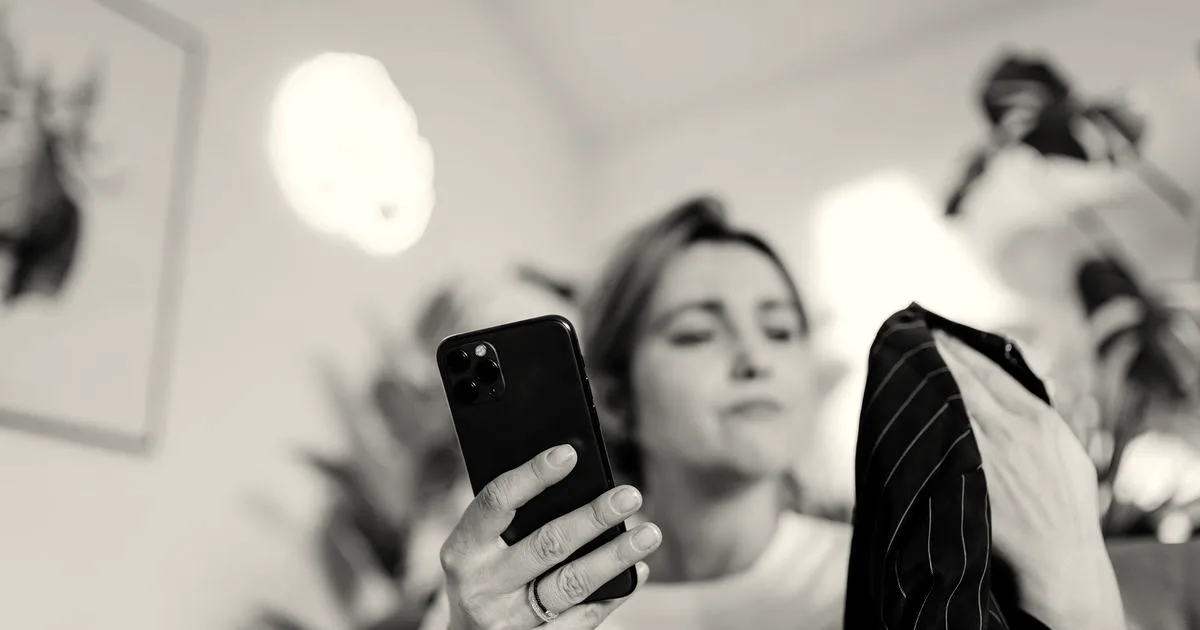 A woman looks at her smartphone while examining a dark striped garment for live shopping