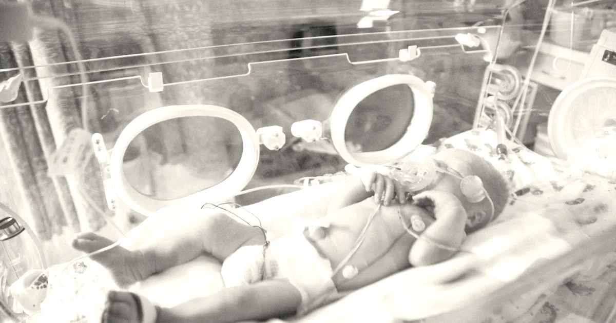 A premature infant receiving medical care inside a hospital neonatal incubator.
