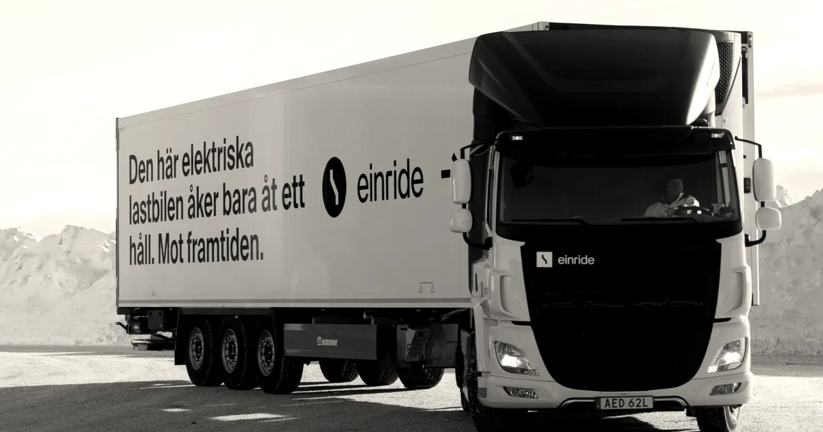 An Einride white electric transport truck driving on an open road with mountains in the background.