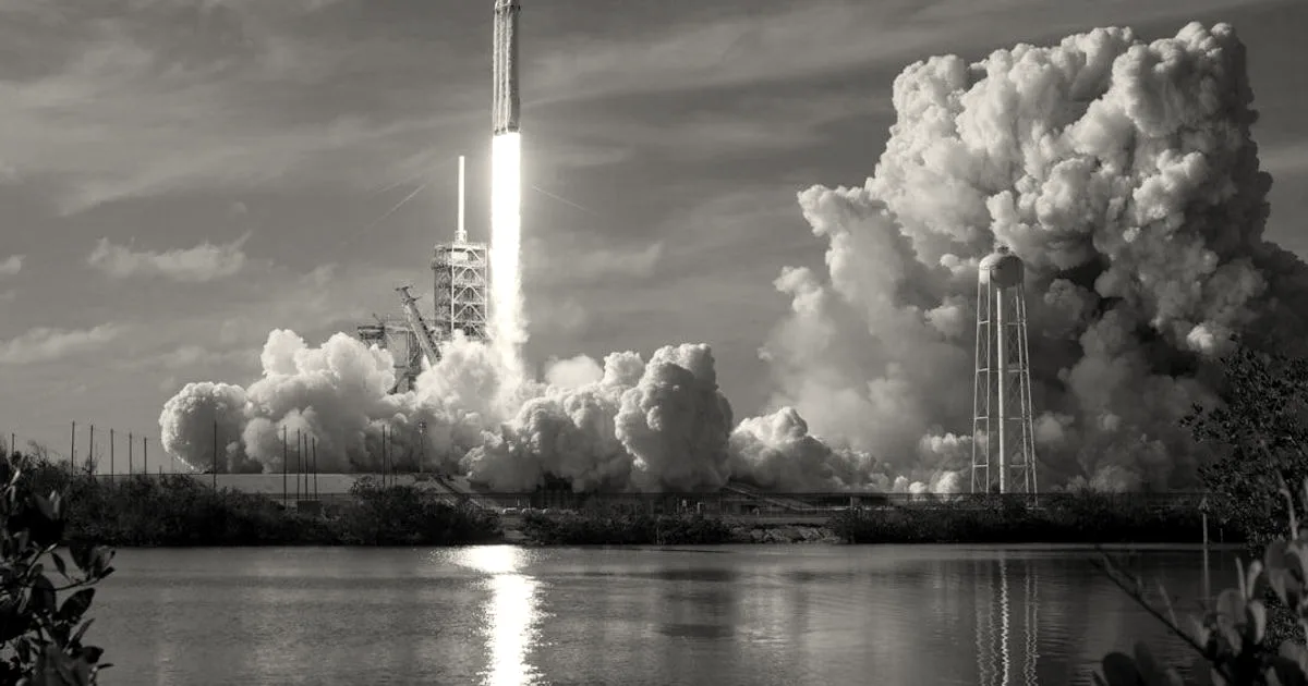 SpaceX Falcon Heavy rocket launching from a launchpad with huge plumes of smoke and water reflection