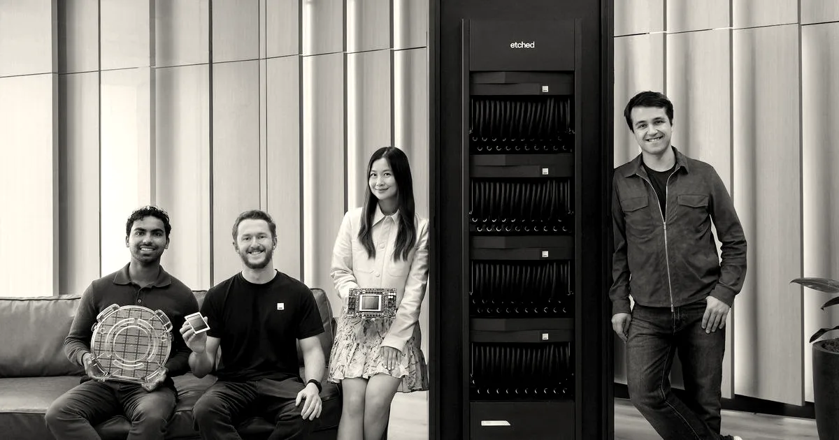 Four people posing next to a tall black server rack holding semiconductor hardware.