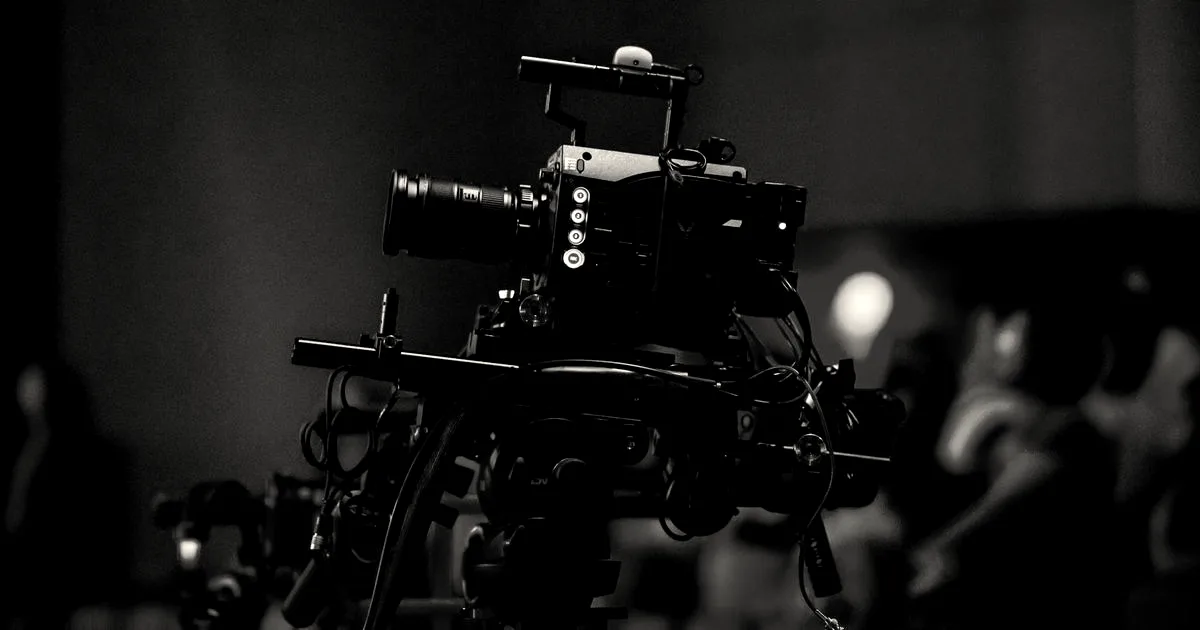 A professional video camera setup recording a live event on a illuminated stage with an audience.
