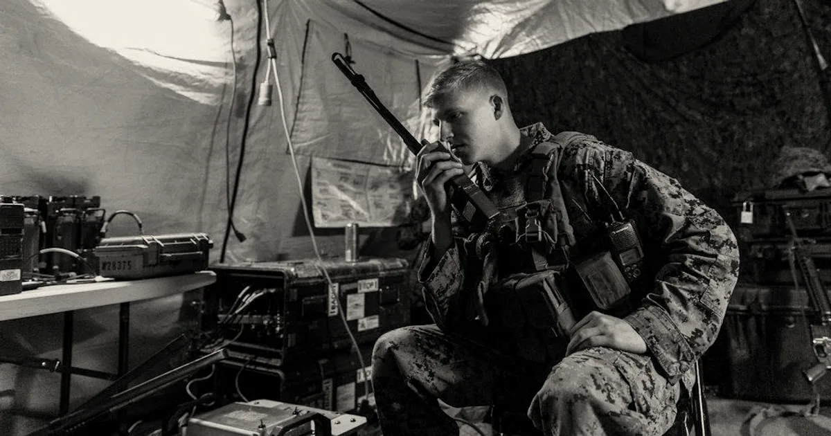 A tactical military communications operator using a radio inside a command tent filled with electronic equipment