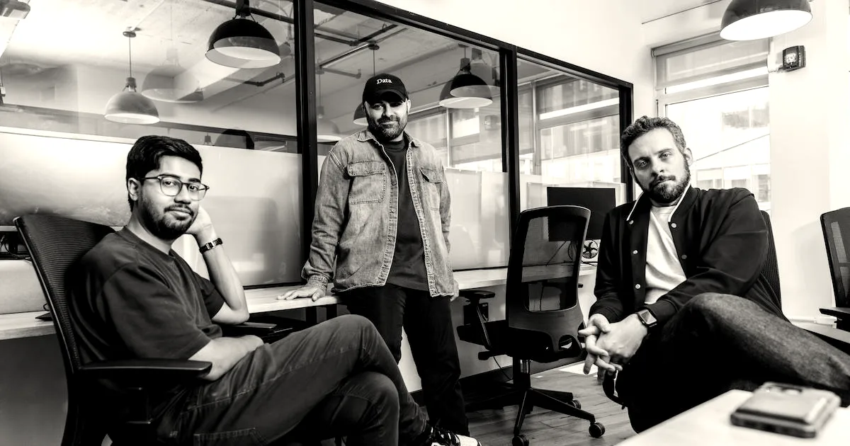 Three male co-founders sitting and standing together in a modern office space.