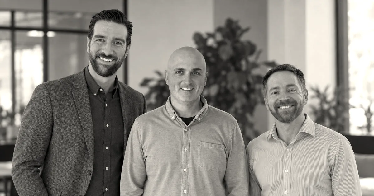 Three male co-founders smiling together standing side-by-side in an office setting.