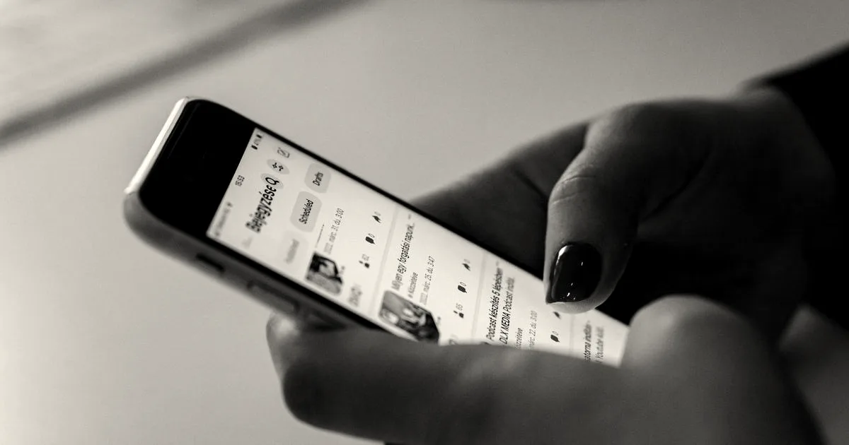 Close-up of a person holding and scrolling on a smartphone displaying a social media feed.