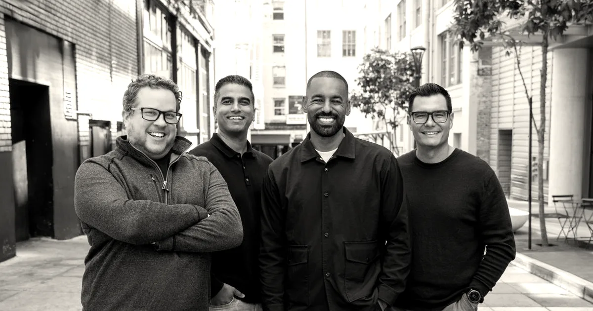 Four men standing together outside on a city street smiling at the camera.