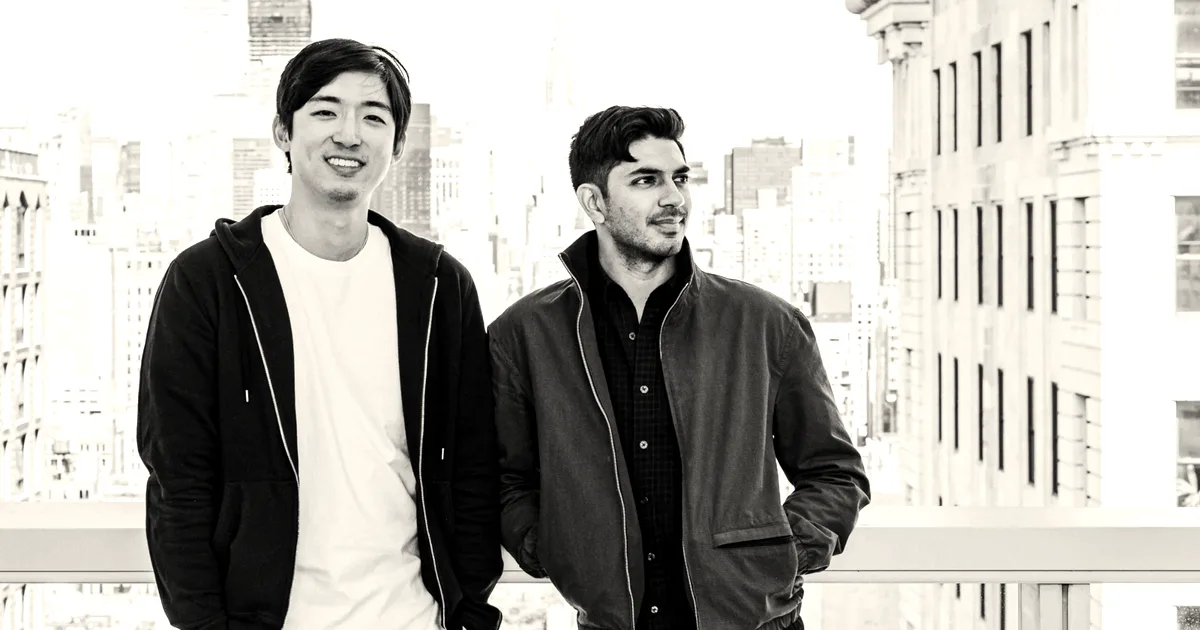 Two men standing against a city skyline backdrop, dressed in casual jackets.