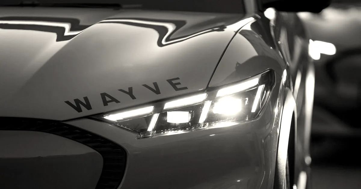 Close-up of a self-driving car headlight and hood displaying the Wayve logo.
