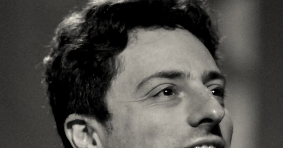 Sergey Brin speaking at a conference event against a dark stage background.