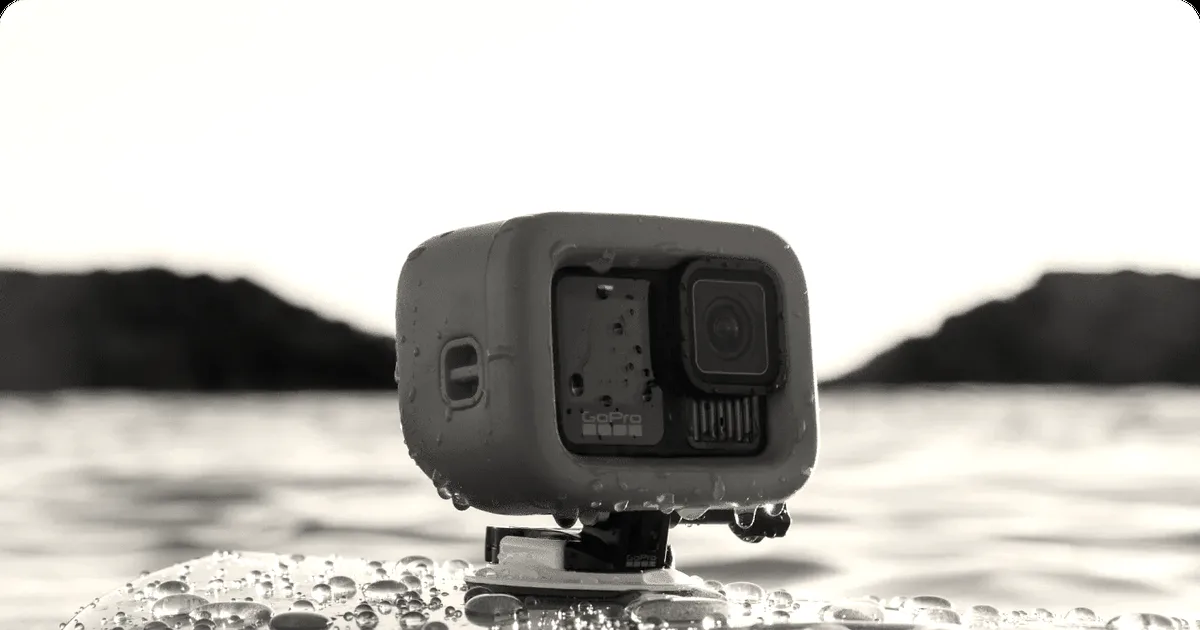 An orange encased GoPro action camera mounted onto the front of a surfboard covered in water droplets.