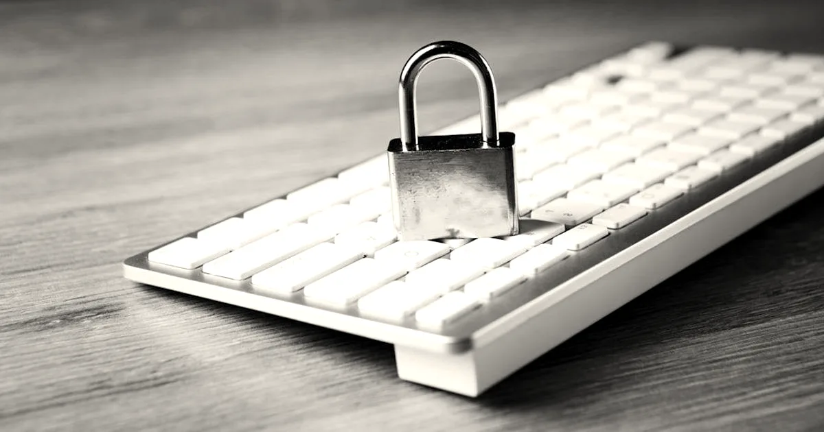 A metal padlock resting on a white computer keyboard atop a wooden desk surface
