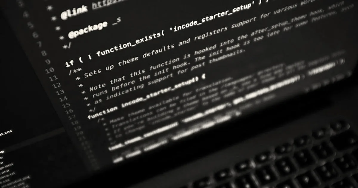 Code displayed across a laptop screen viewed at an angle with an illuminated keyboard in darkness